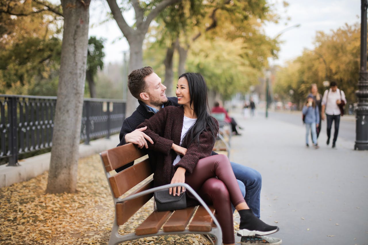 Features Happy couple sitting on a bench in a park during fall, sharing a joyful moment together.